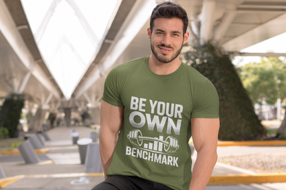 Man wearing a green t-shirt with 'Be Your Own Benchmark' text and graphic, standing outdoors.
